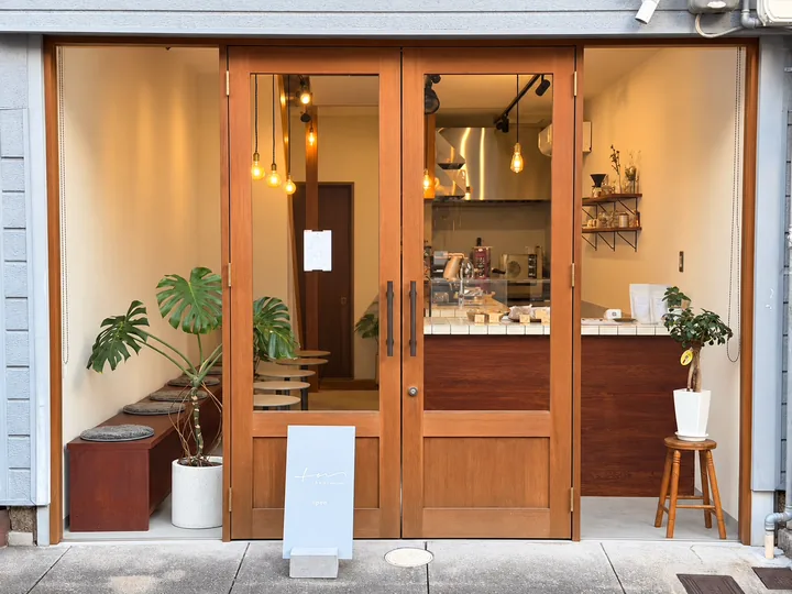 The front of the shop: wooden double doors with glass panes, the lit interior with bulb lights, a white tiled counter and plants, and an “open” sign by the door