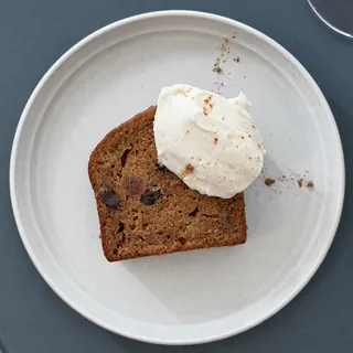 青灰色の丸テーブルの上、生成りの丸皿にのった、クリームを添えたキャロットケーキ